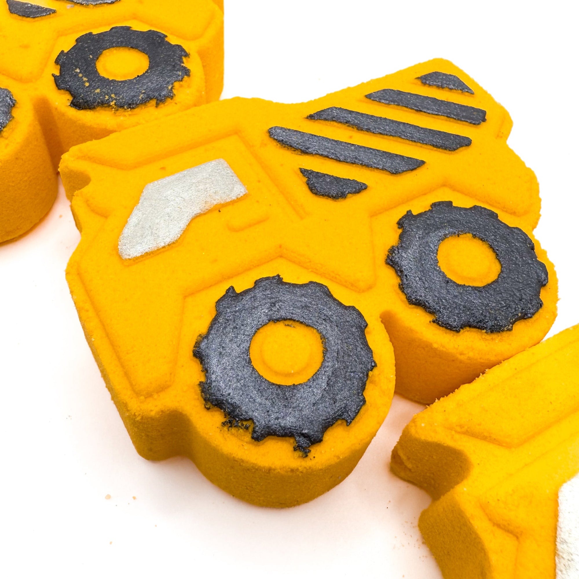 Yellow dump trucks bath bombs made by Rusted Acre soap Co. Black hand painted stripes and other details, one laying down full view.