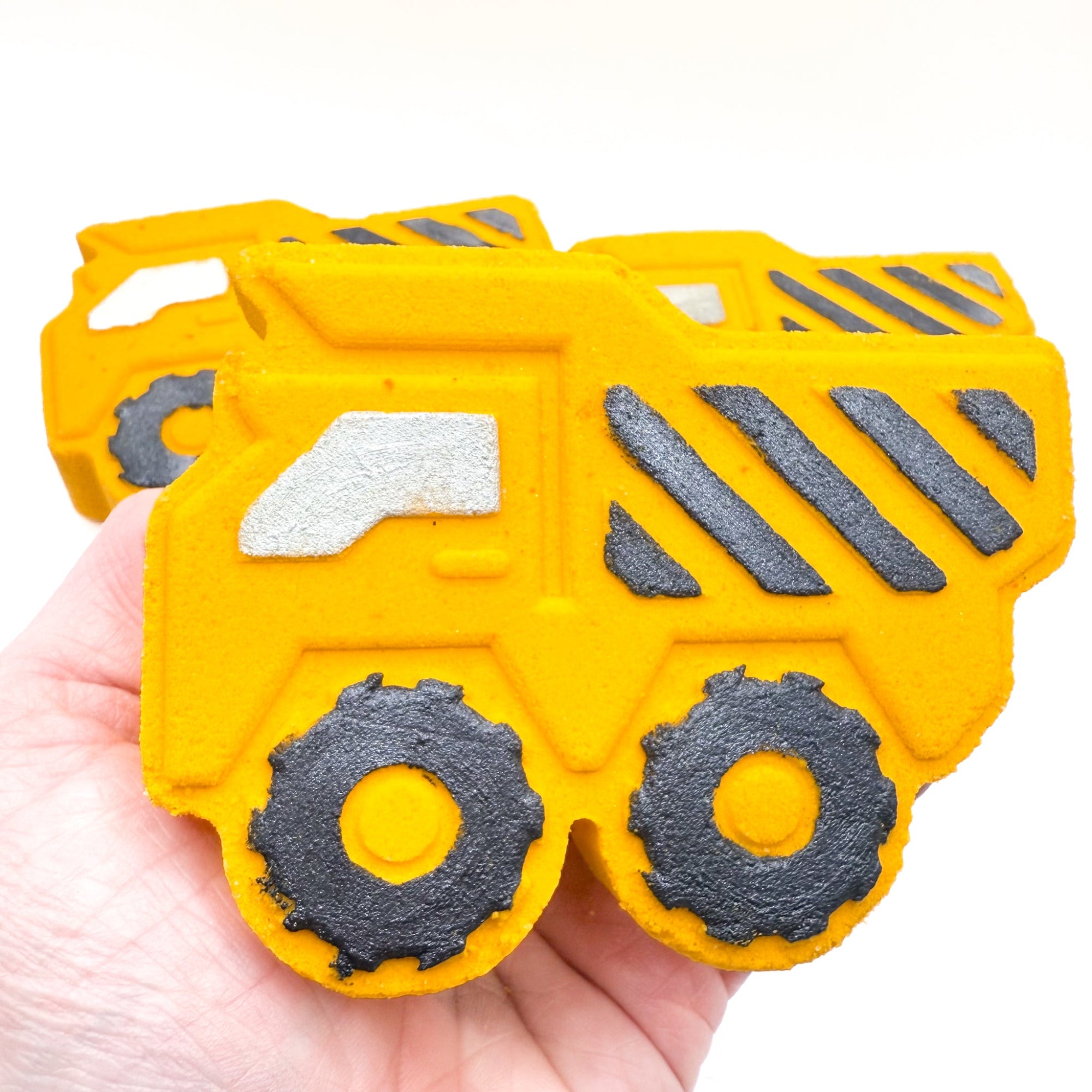 Yellow dump trucks bath bombs made by Rusted Acre soap Co. Black hand painted stripes and other details, up close view being held in a hand.