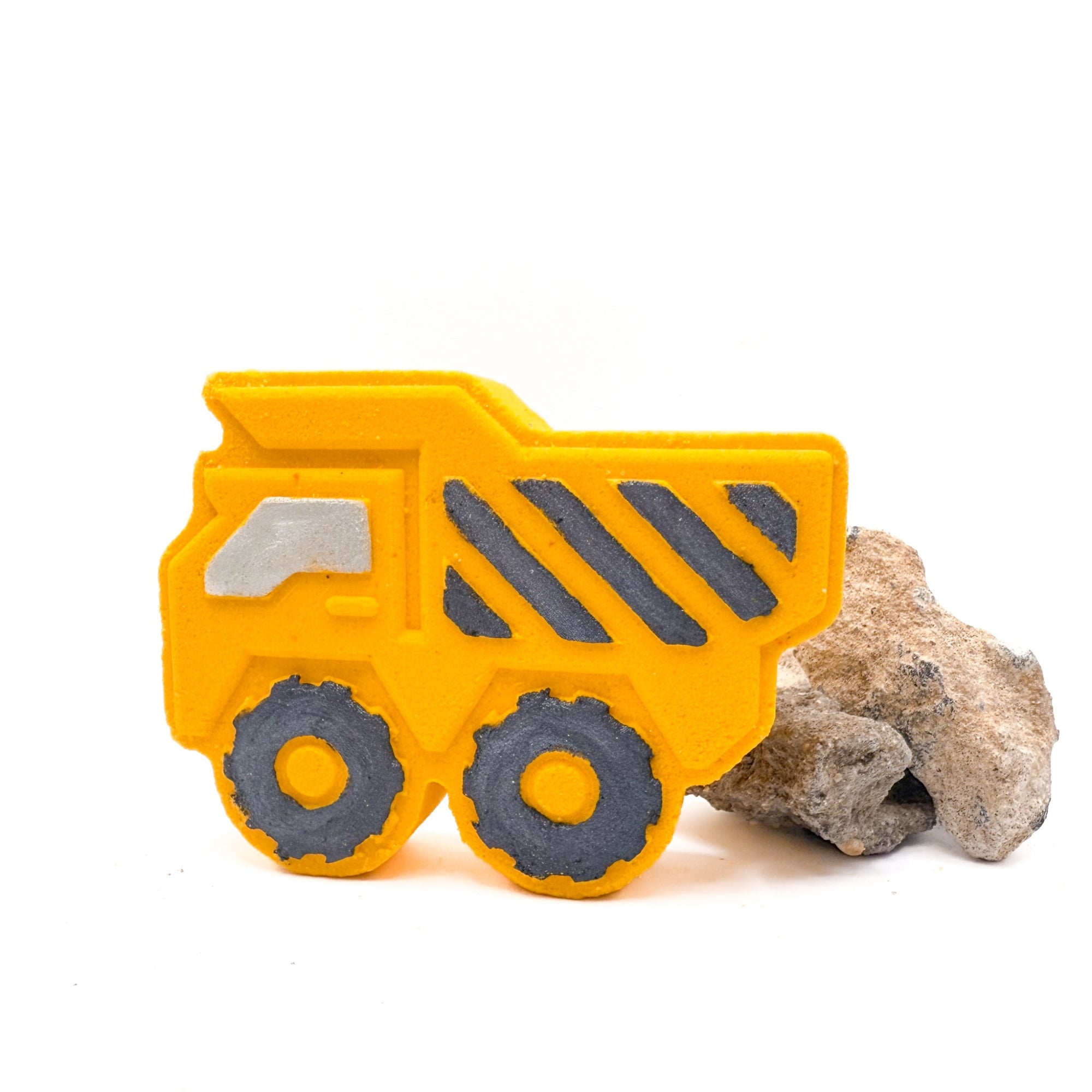 Yellow dump trucks bath bombs made by Rusted Acre soap Co. Black hand painted stripes and other details, standing up with rocks behind it.