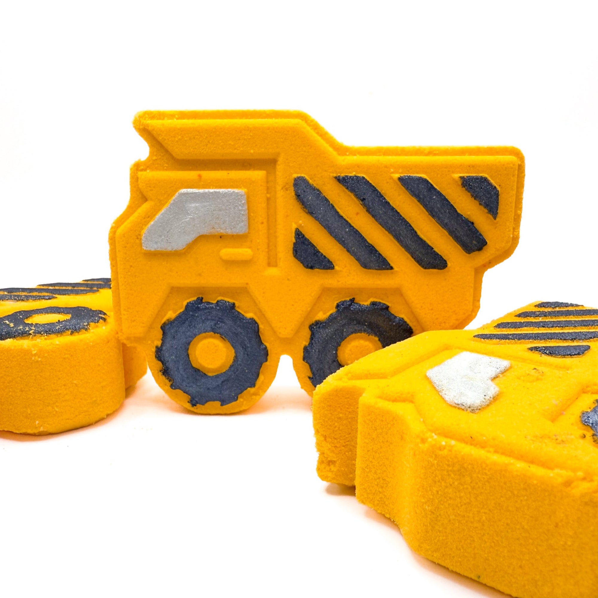 Yellow dump trucks bath bombs made by Rusted Acre soap Co. Black hand painted stripes and other details, one standing up two, laying down. 