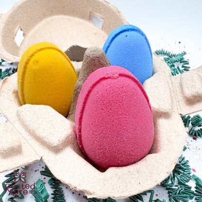 Three colorful egg shaped bath bombs in a heart shaped carton for easter made by Rusted Acre Soap Company. 