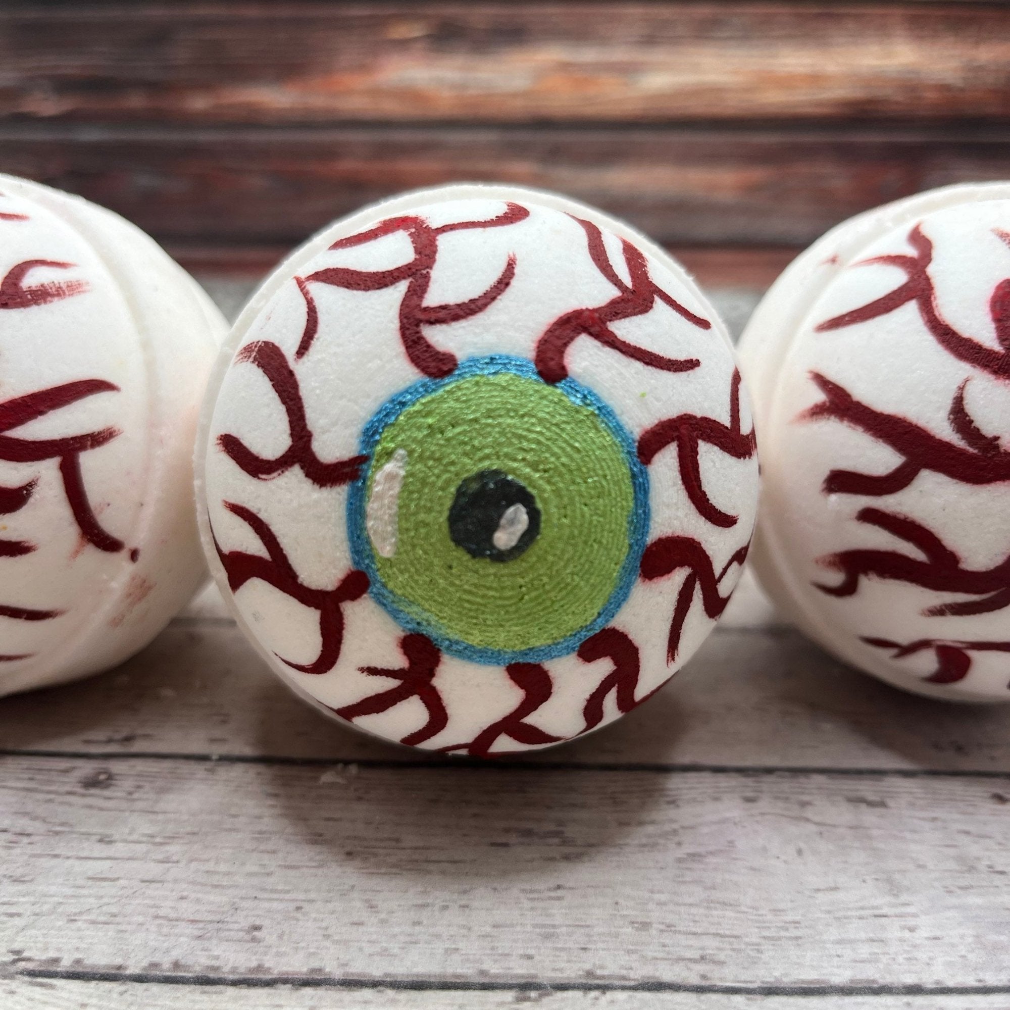 Three round white bath bombs hand-painted green eye, teal outline and red veins. 