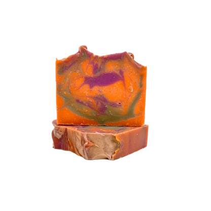 Two bars of fruity cereal handmade soap from Rusted Acre Soap Co. One lying flat one upright. The colors are bright orange, purple and green swirled together. 