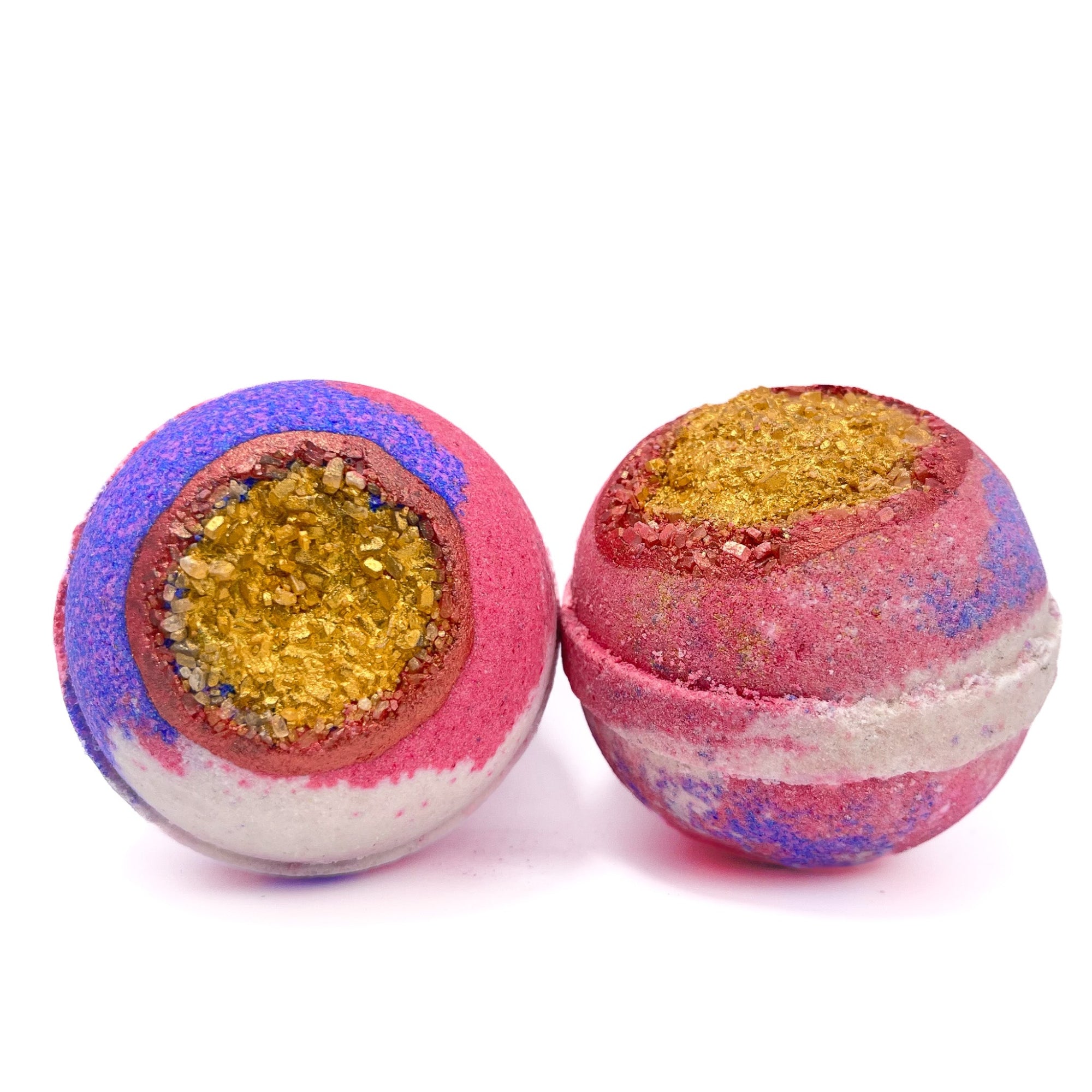Two purple, white, and red round bath bombs side by side. Embedded with gold dusted Epsom salt. Hand-painted red ring around the gold. Made by Rusted Acre Soap Co.