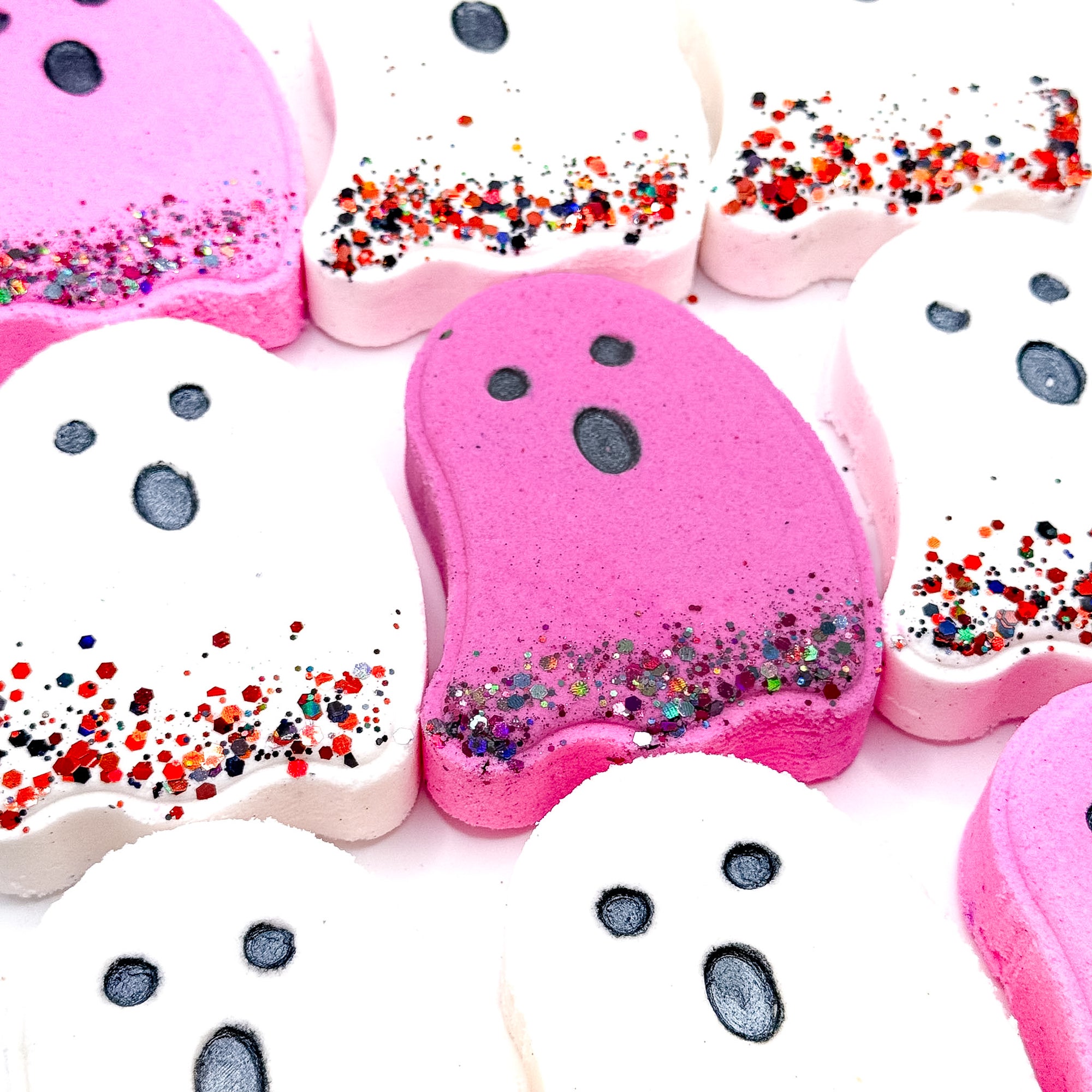 Assorted pink and white ghost-shaped Halloween bath bombs from Rusted Acre Soap Co., each with black eyes and glittery bottoms.