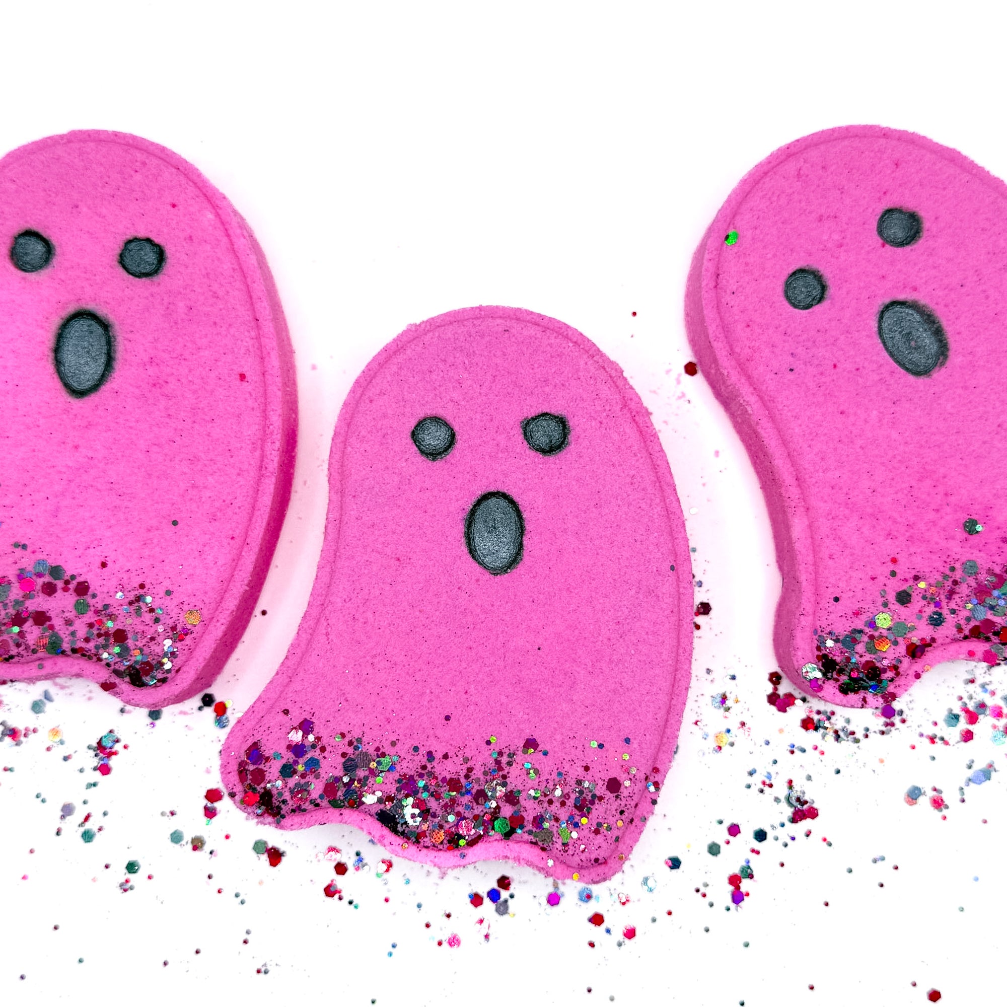 Three bright pink ghost-shaped Halloween bath bombs from Rusted Acre Soap Co. with black eyes and glittery bottoms — a playful spooky-season treat.