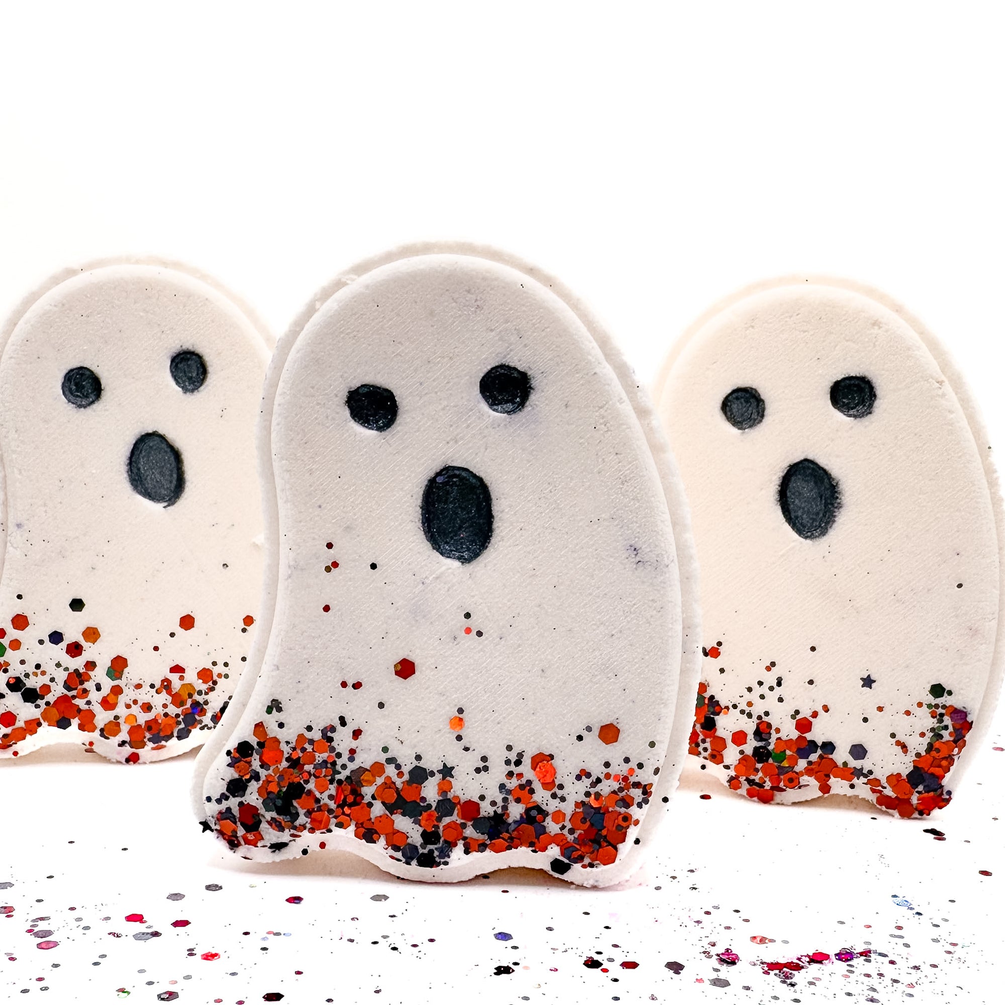 Three white ghost-shaped Halloween bath bombs from Rusted Acre Soap Co. with black eyes, open mouths, and red-orange glitter at the base.