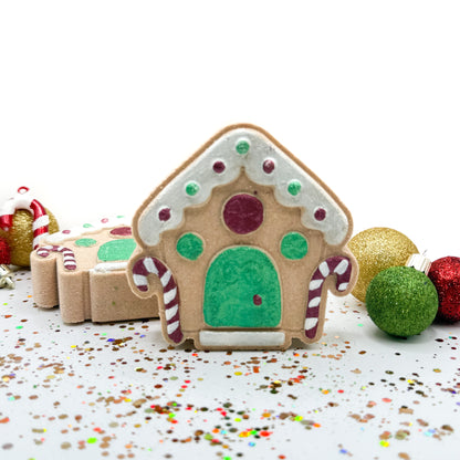 Front and side view of hand painted gingerbread house bath bombs with Christmas ornaments in the background. 