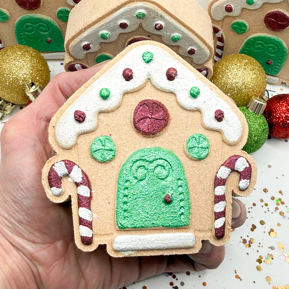 Hand painted gingerbread house bath bomb being held in a hand to show size and details. 