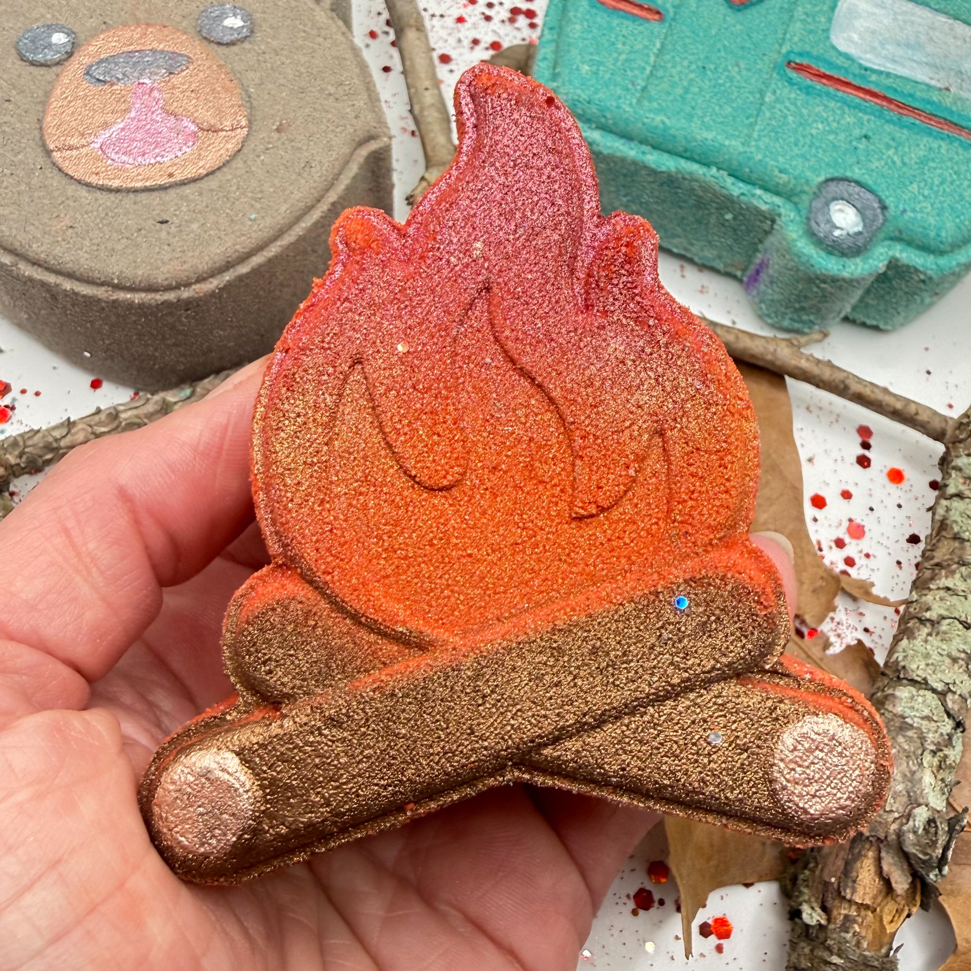 Hand holding a campfire shaped bath bomb with a colorful gradient on a decorative background.