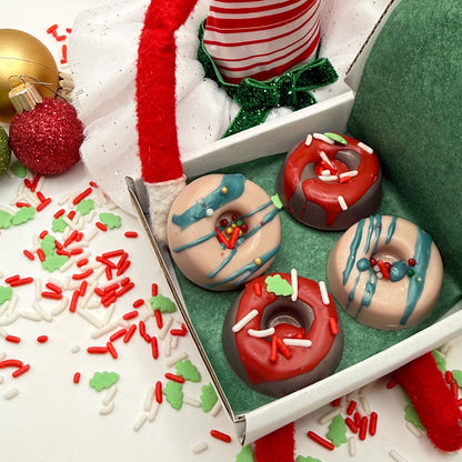 Box of 4  red and green min donut soaps handmade by Rusted Acre Soap Co on a white background with Christmas themed decorations. 