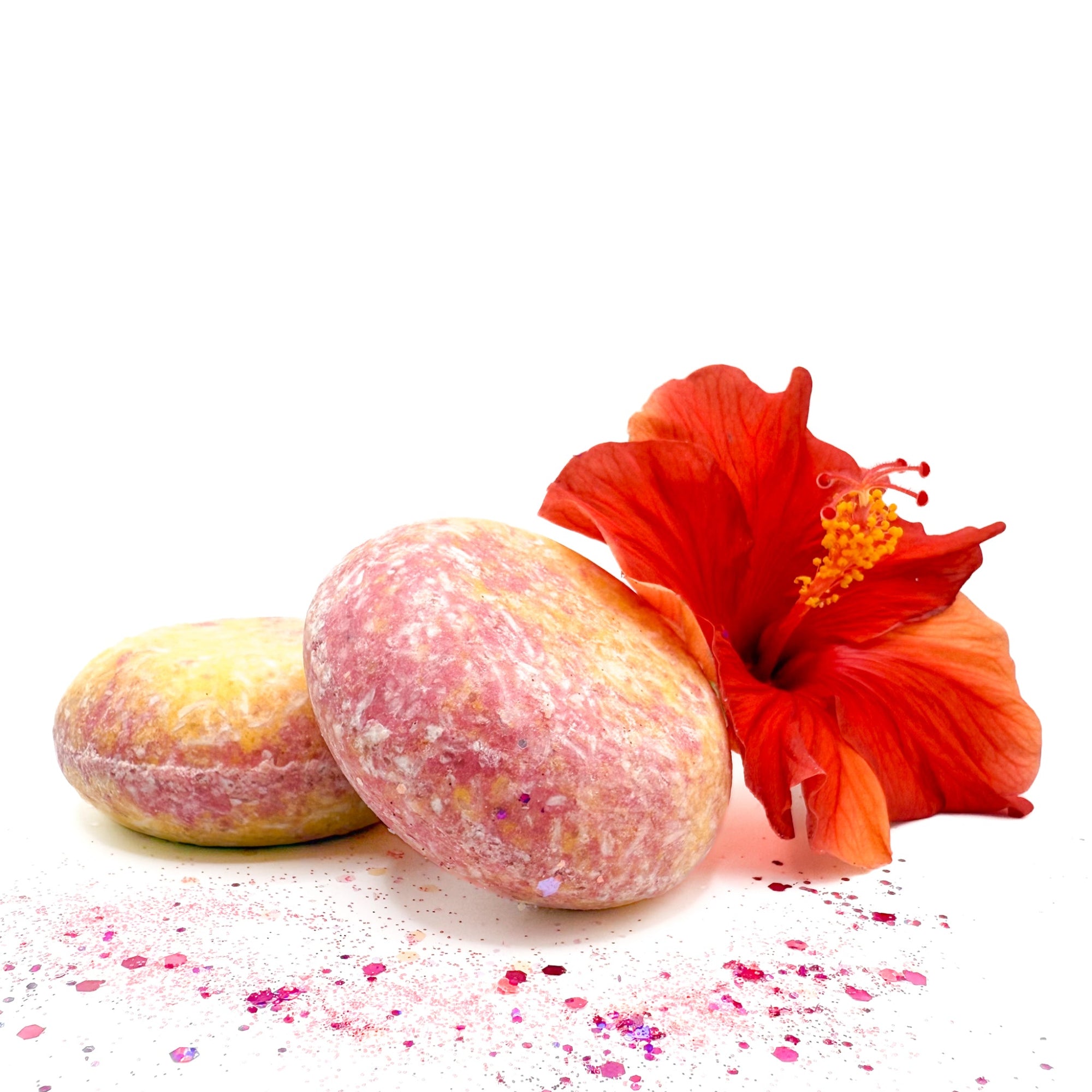 Two island hibiscus shampoo bars from Rusted Acre Soap Company displayed with a red hibiscus flower.