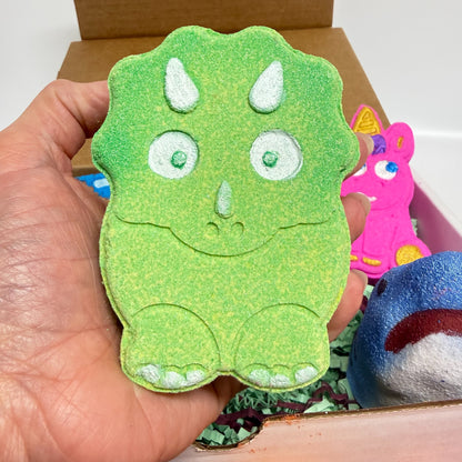 Green dinosaur bath bomb being held in a hand with other bath bombs in the back ground. 