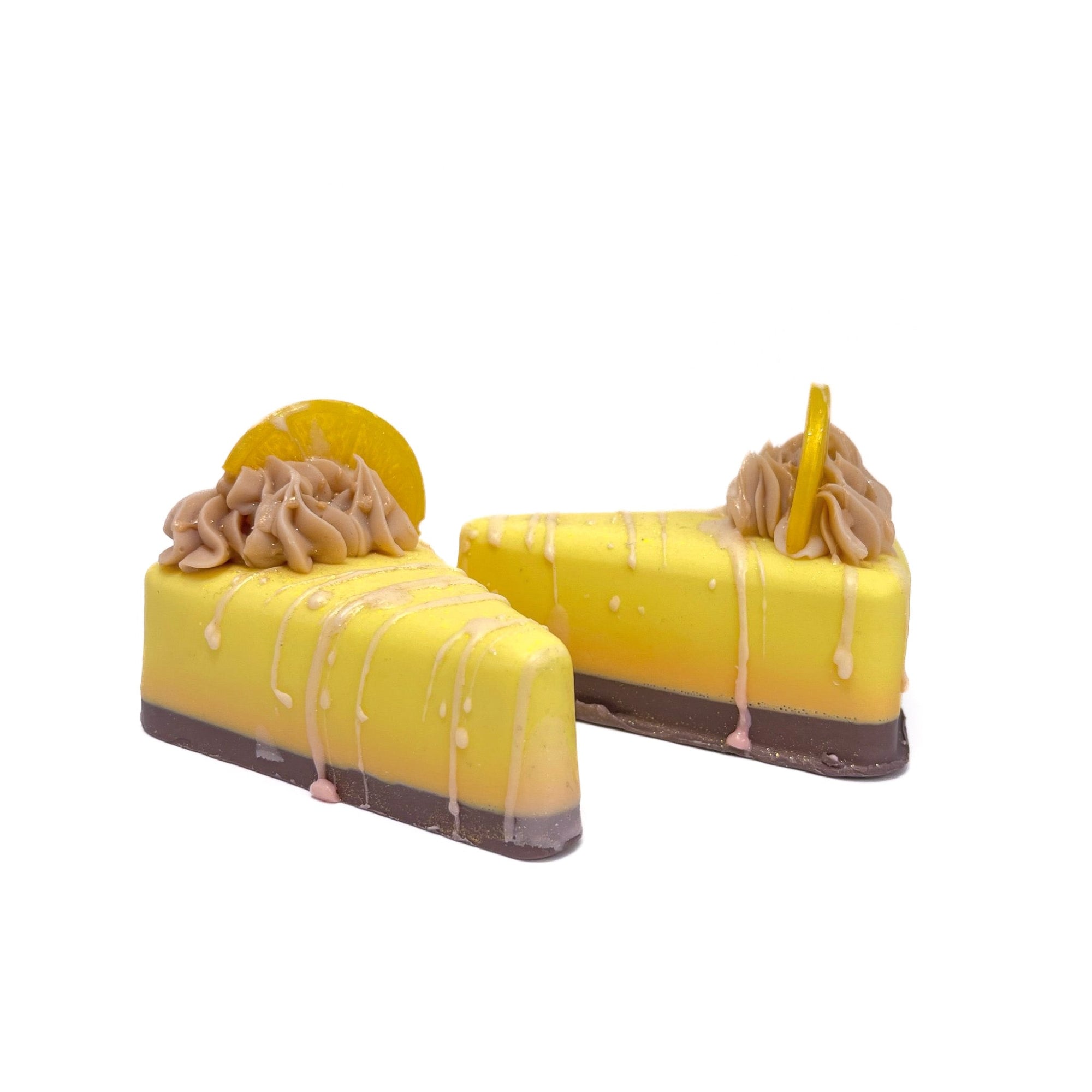 Two slices of pie shaped lemon yellow soap topped with a puff of cream colored soap frosting and a slice of lemon shaped soap and white drizzle. 