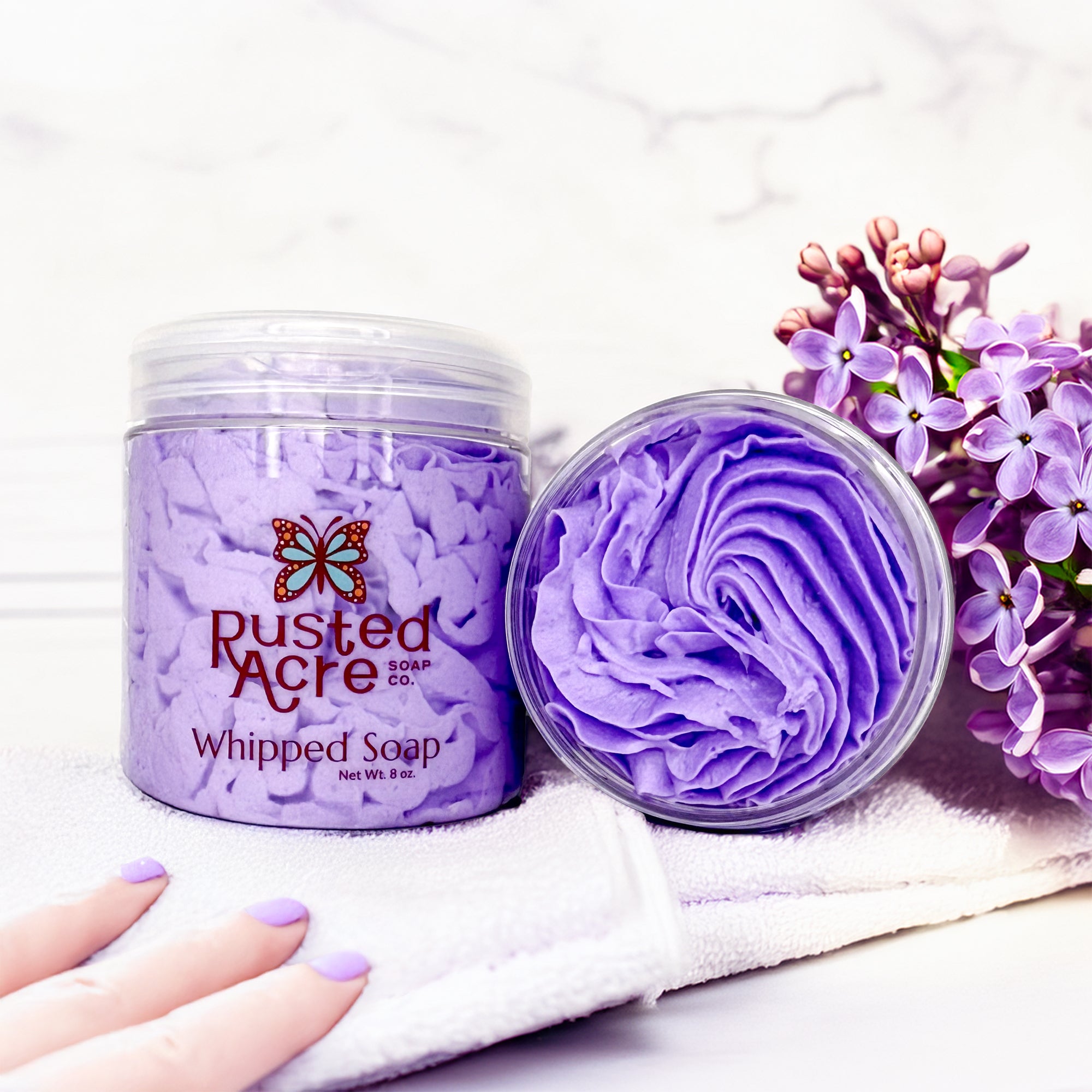Two jars of lilac whipped soap in a life style setting.