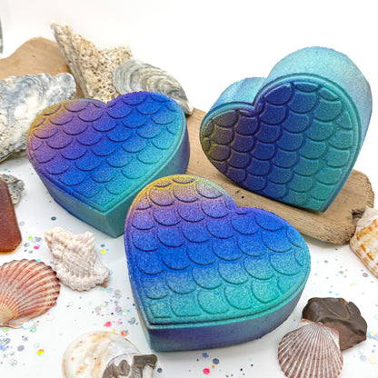 Three heart shaped bath bombs with mermaid scale design on a white background with seashells.