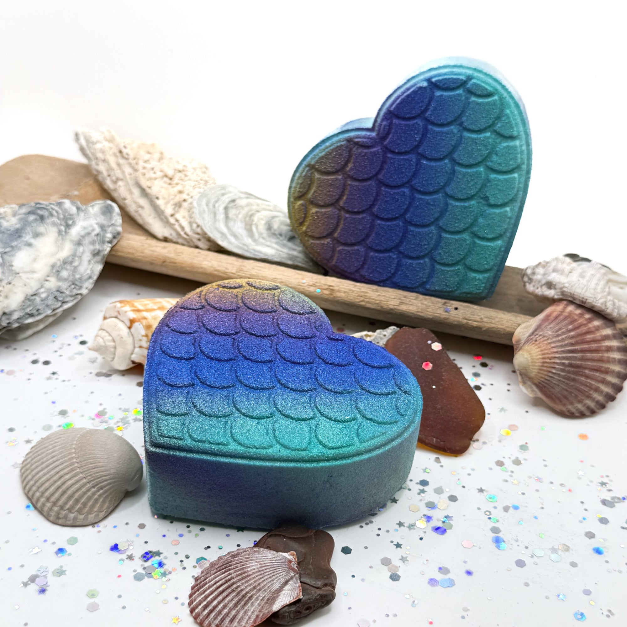Two heart shaped mermaid scaled bath bomb with seashells on a white background