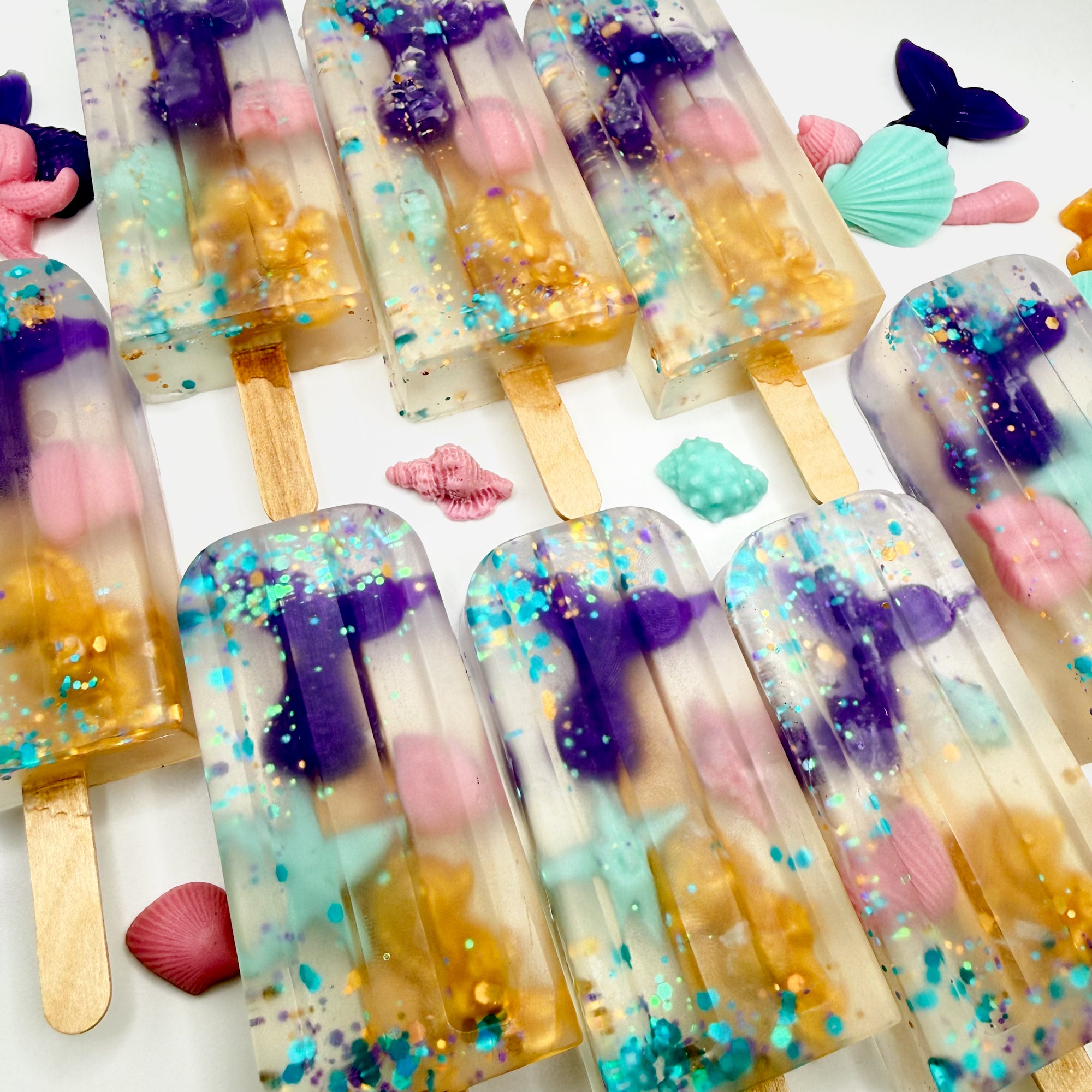 Multiple hand poured mermaid popsicle shaped soaps with mermaid soap embeds inside of clear soap. 
