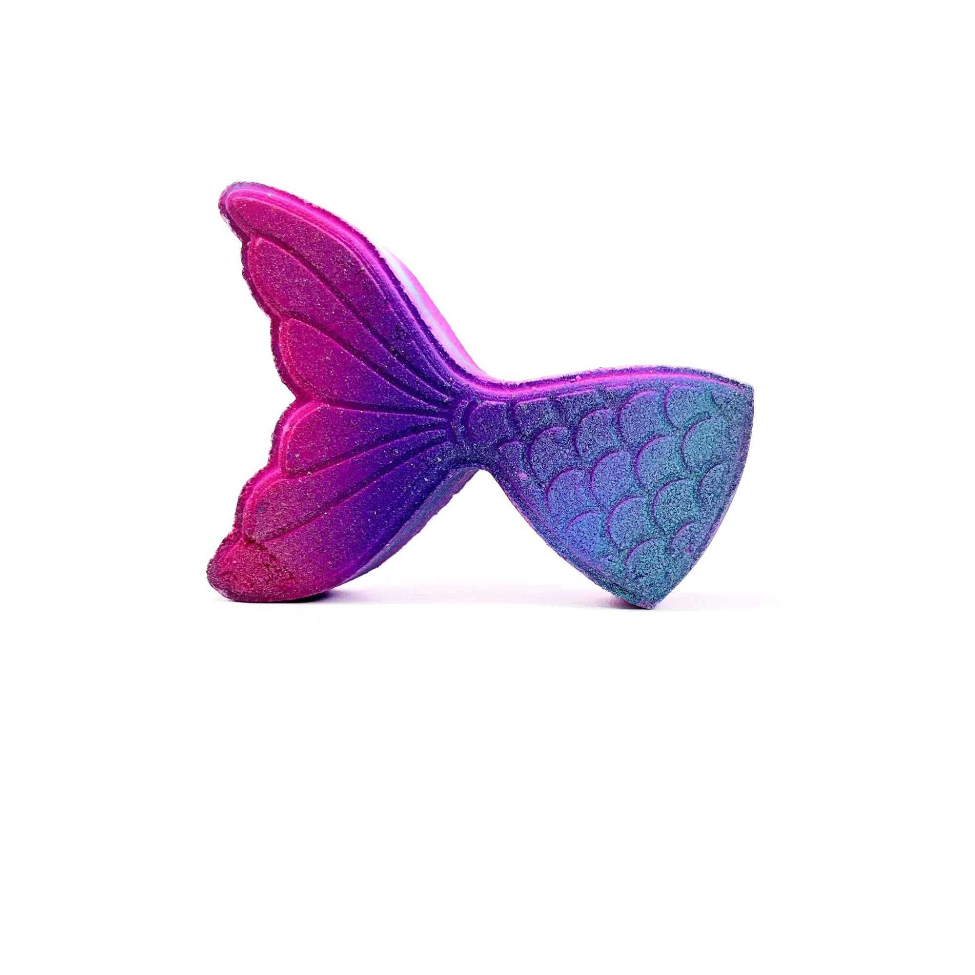 A pink and teal swirled mermaid tail shaped bath bomb from Rusted Acre Soap Company lying on its side. 