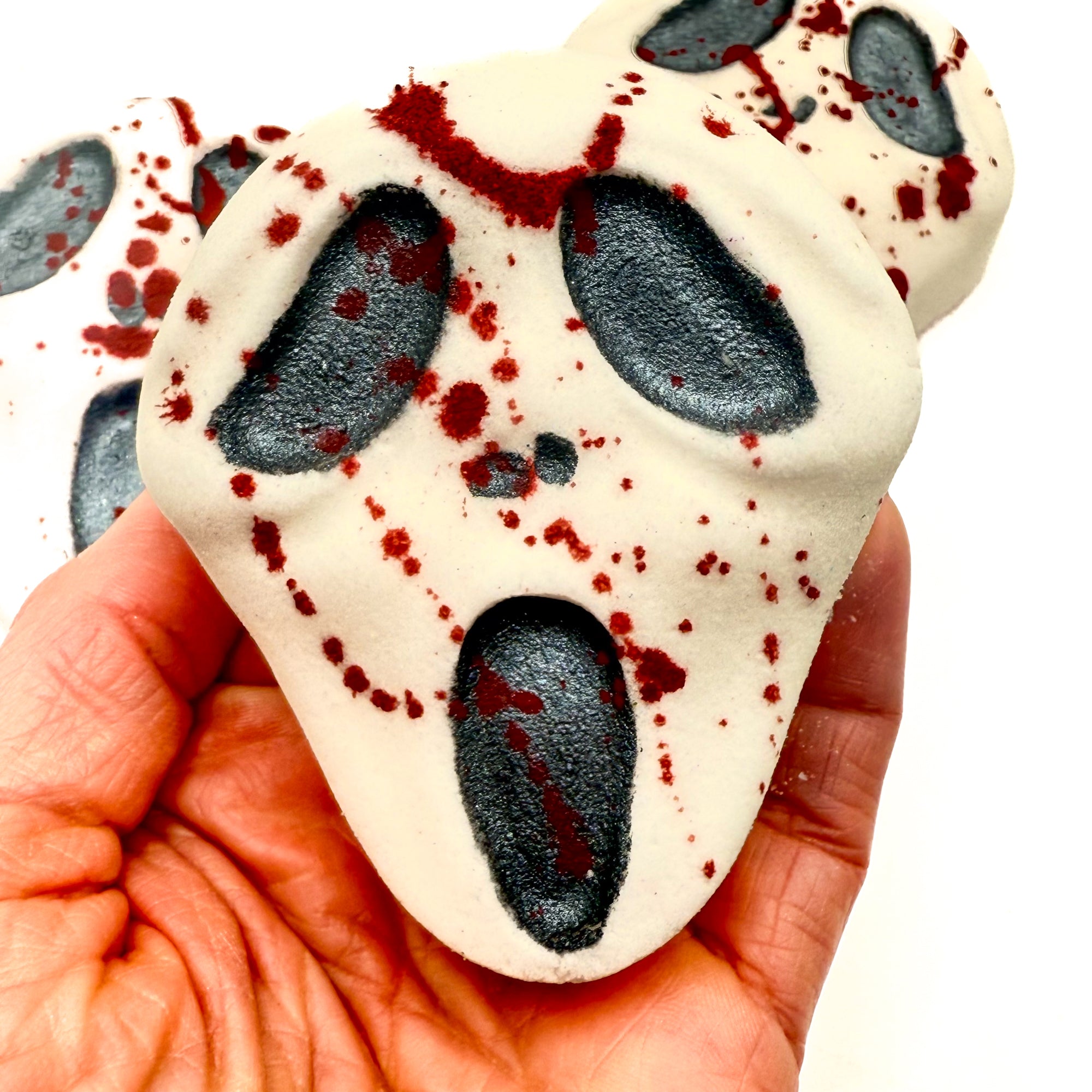 Close-up of Midnight Caller bath bomb held in hand, showing black eyes, mouth, and dramatic red blood-like splatters. Handmade by Rusted Acre Soap Company. 