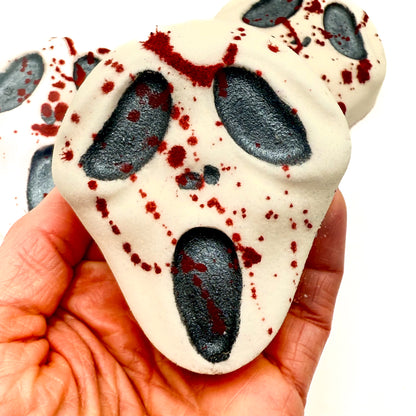 Close-up of Midnight Caller bath bomb held in hand, showing black eyes, mouth, and dramatic red blood-like splatters. Handmade by Rusted Acre Soap Company. 