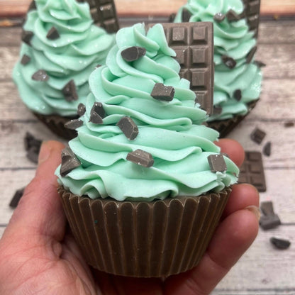 One hand piped and decorated mint chocolate chip cupcake soap being held in a hand. Soap is decorated with soap “chocolate chips” and a little soap chocolate bar. 