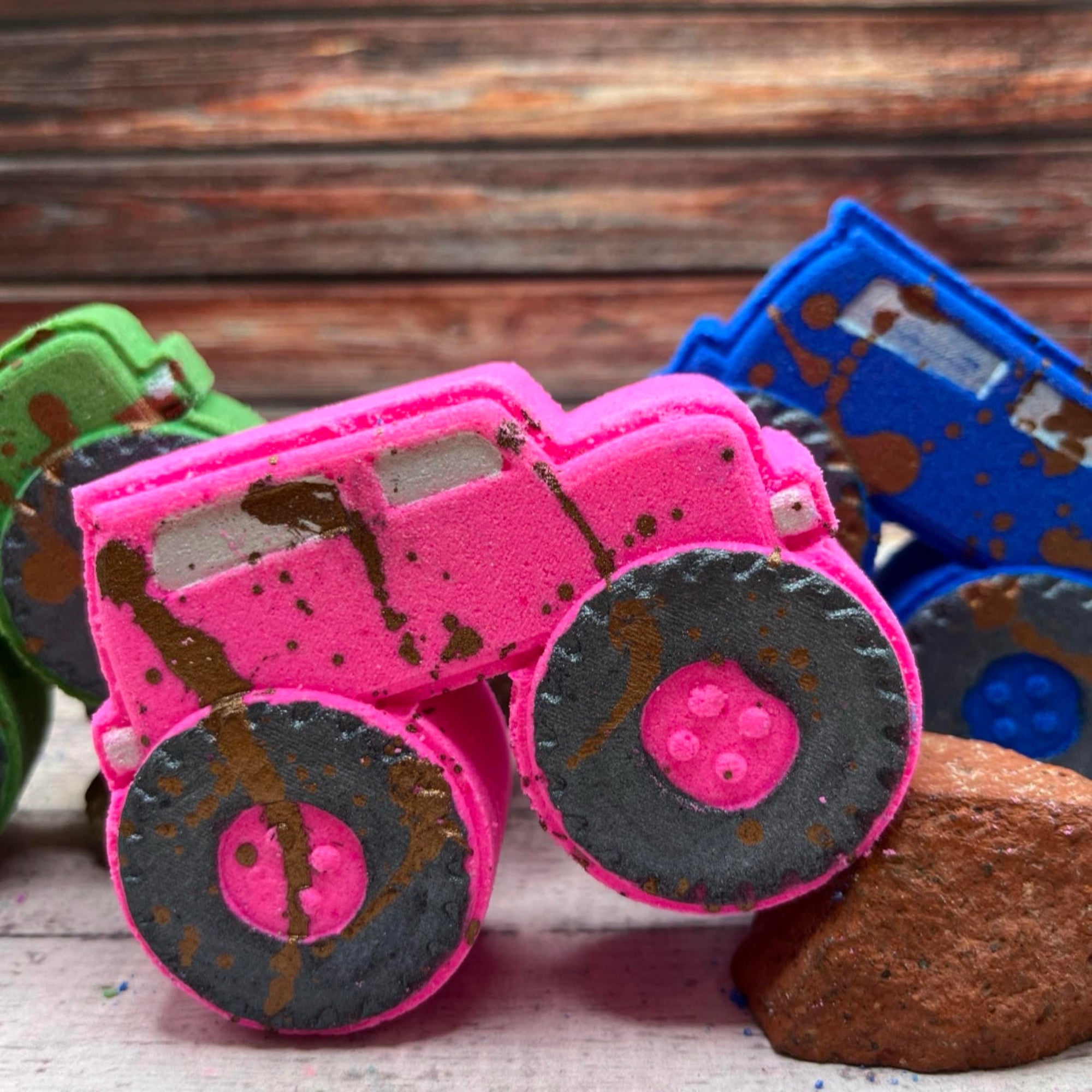 A pink monster truck bath bomb with hand-painted black wheels and muddy brown splashes, hand painted to look like it just powered through the dirt. A fun bath bomb for kids and truck lovers.