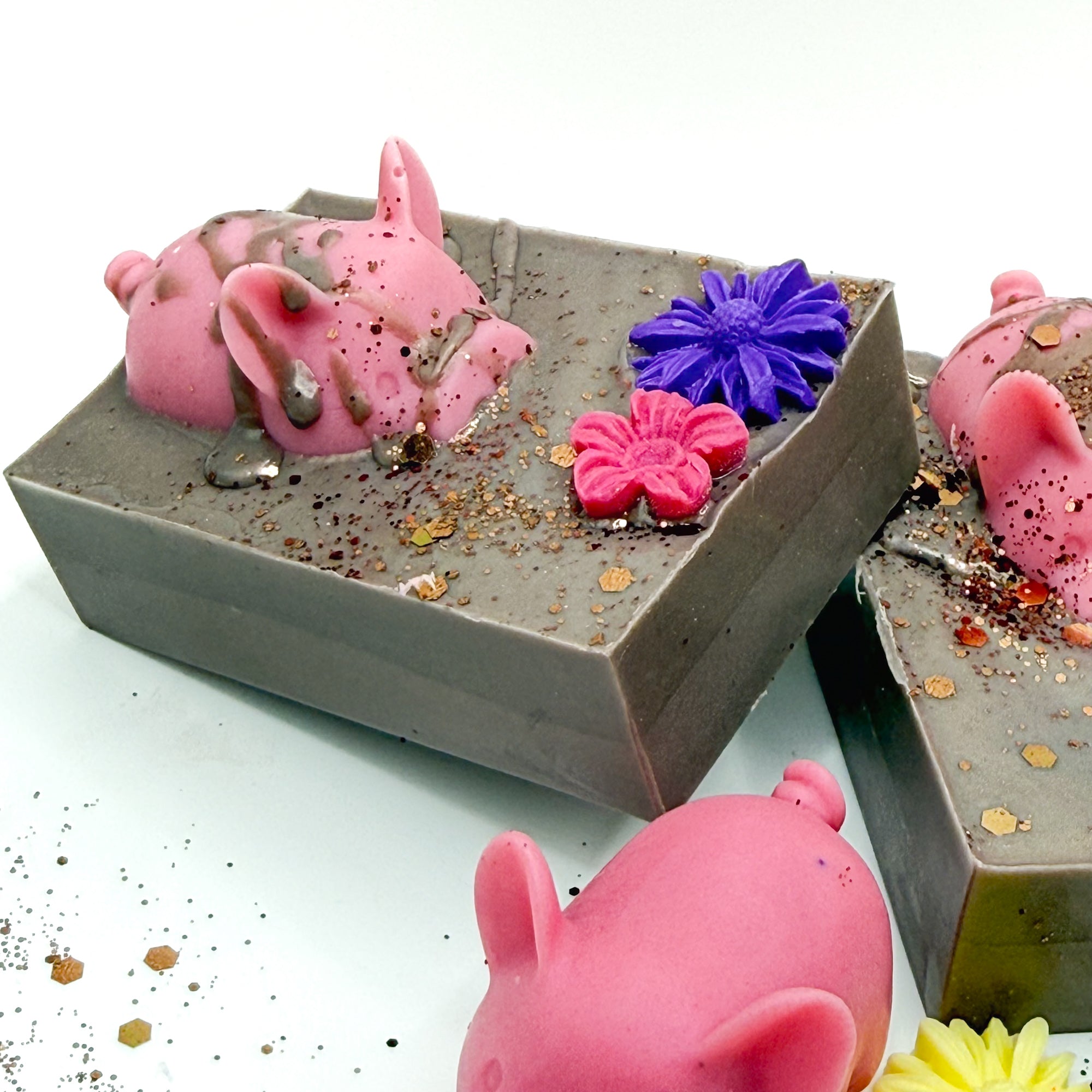 Side view of a hand made decorative soap with pink pig and flowers in a brown mud looking soap base. 
