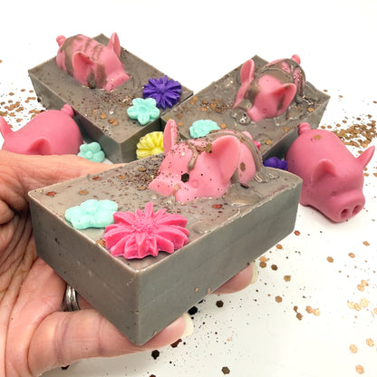 Hand made decorative soap with pink pig and flowers in a brown mud looking soap held in hand. Hand poured by Rusted Acre Soap Co