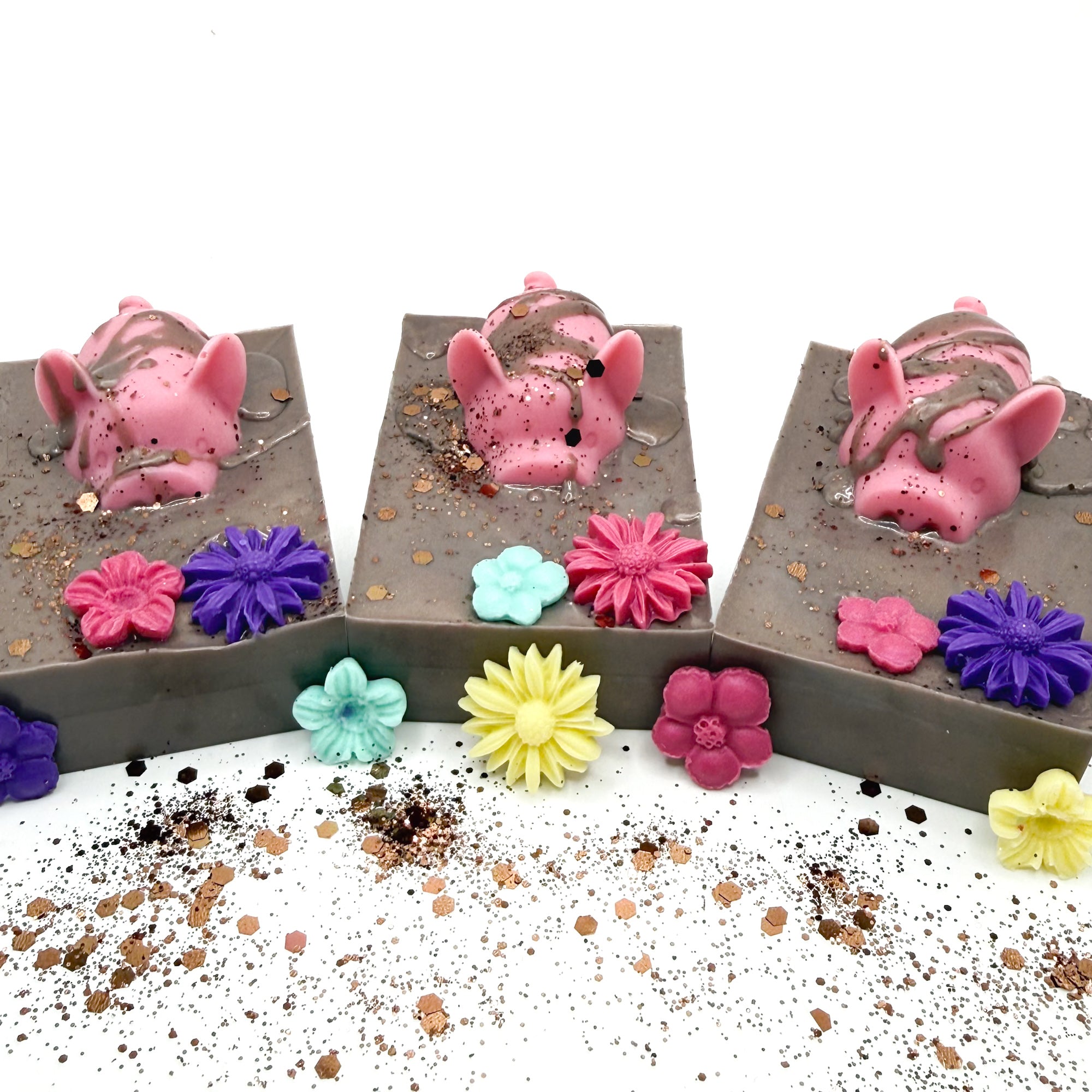 Three hand made decorative soap with pink pig and flowers in a brown mud looking soap. 