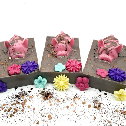 Three hand made decorative soap with pink pig and flowers in a brown mud looking soap. 