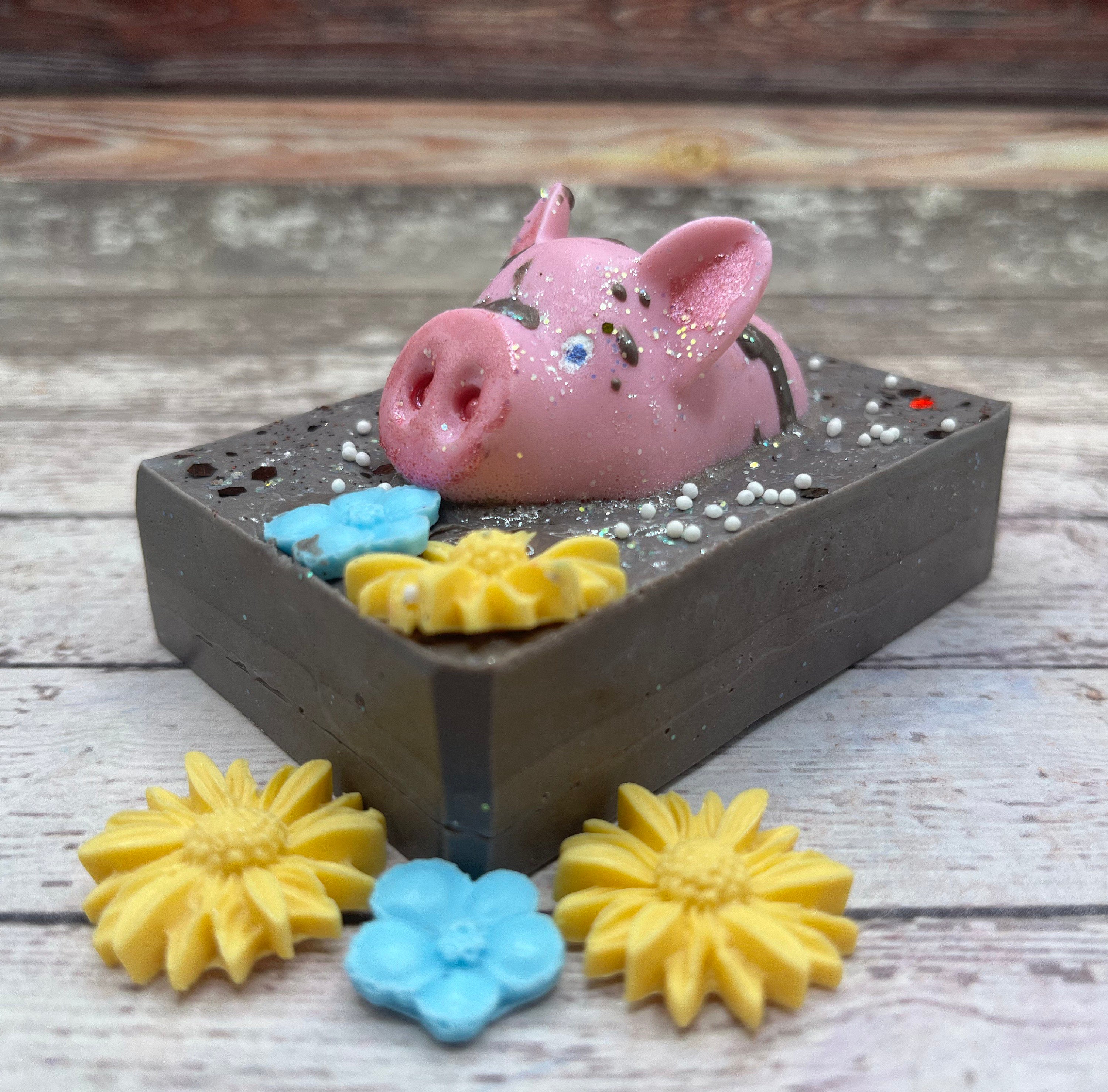 Brown bar of soap with pink pig soap embedded, drizzled with "mud". Decorated with 1 blue and 1 yellow flower.