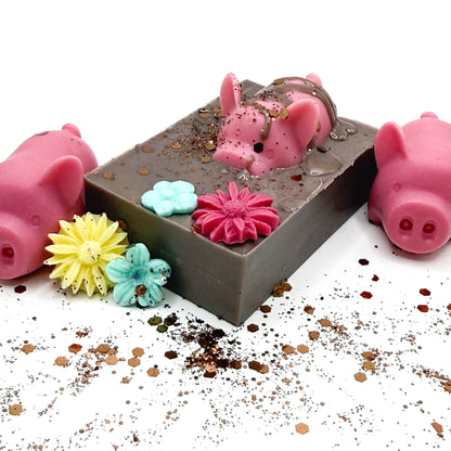Brown bar of soap with pink pig soap embedded, drizzled with "mud". Decorated with 1 blue and 1 yellow flower.