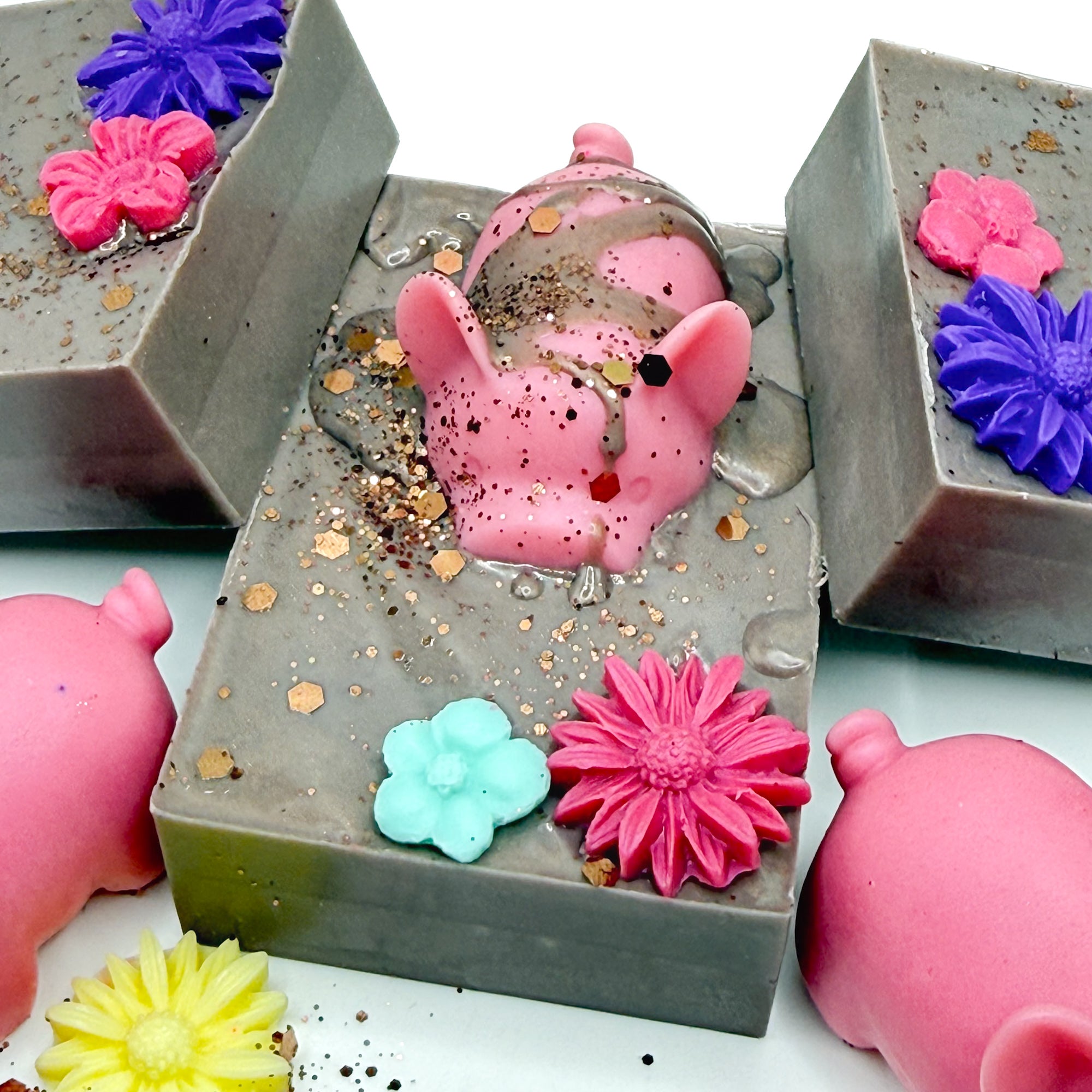 Top view of a hand made decorative soap with pink pig and flowers in a brown mud looking soap. 