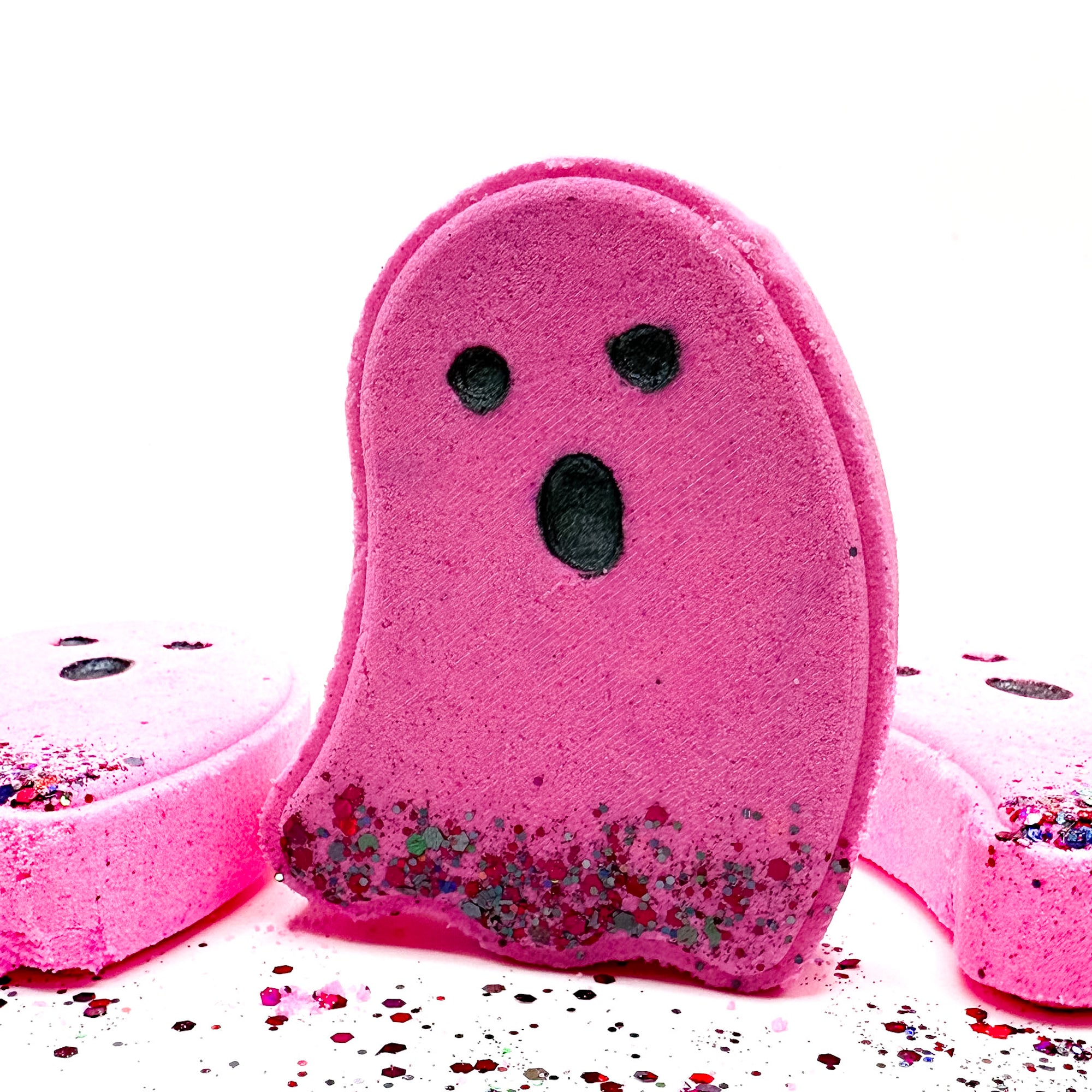 Pink ghost-shaped bath bomb from Rusted Acre Soap Co. with black eyes, a surprised mouth, and glitter base 
