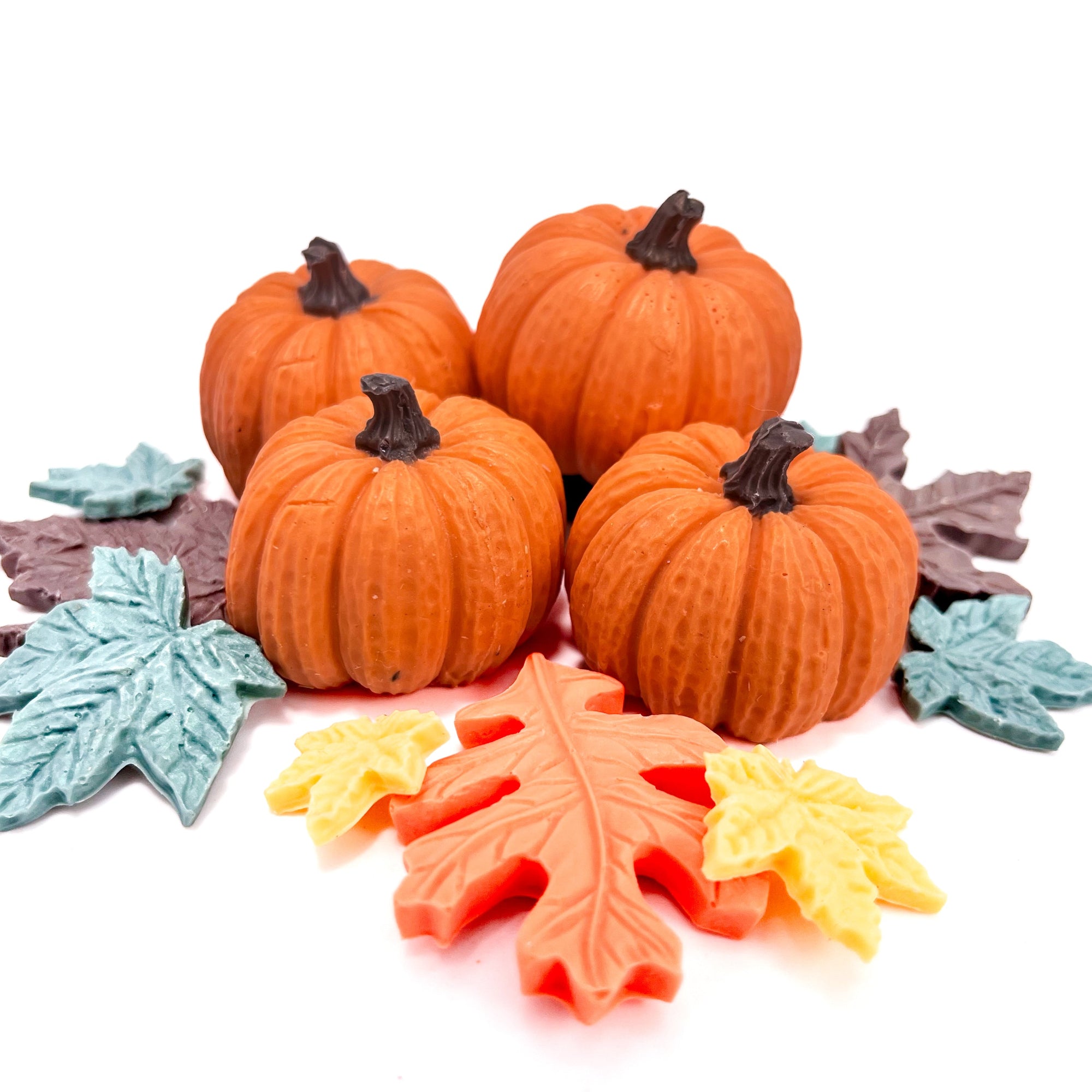 Four orange pumpkin soaps with brown stems surrounded by colorful leaf-shaped candies on a white background