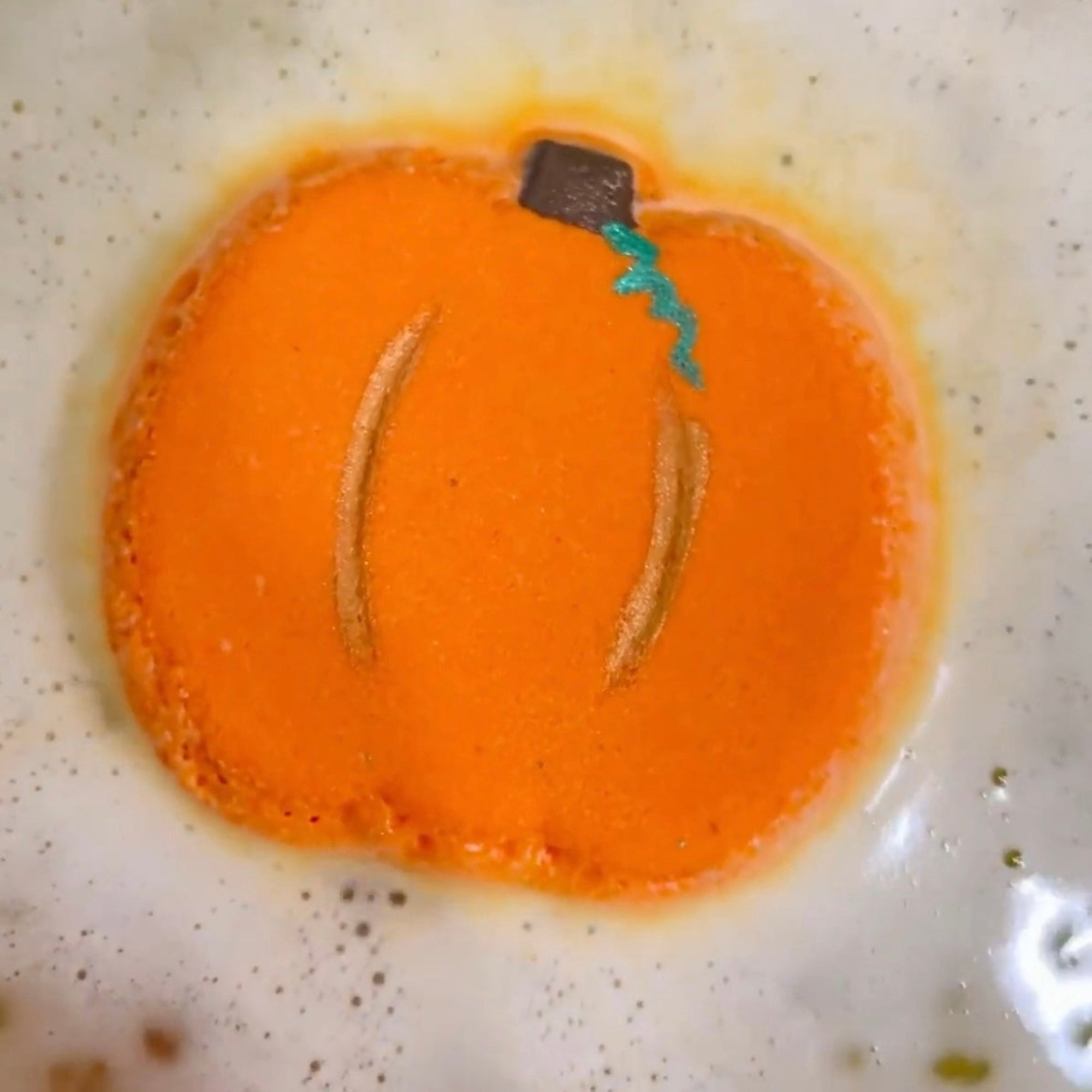 Pumpkin-shaped  bath bomb with painted top on a fizzing in the water.