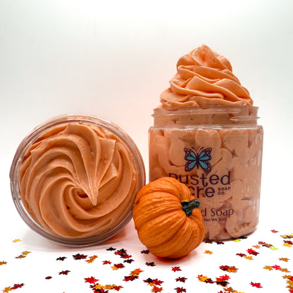 Two jars of orange pumpkin spicewhipped soap with a small pumpkin and fall leaf confetti on a white background.