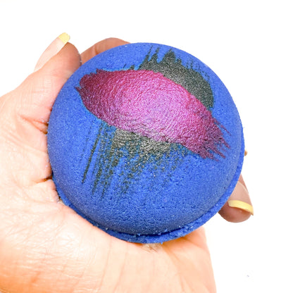 A hand made round purple bath bomb with hand painted brush  strokes on top for detail. Made by Rusted Acre Soap Co.