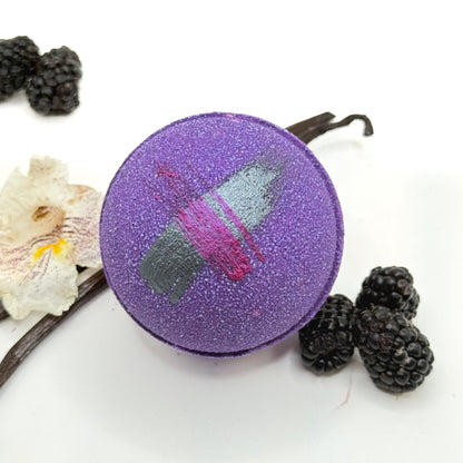 Purple raspberry vanilla bath bomb with a colorful design, surrounded by blackberries and vanilla beans on a white background.