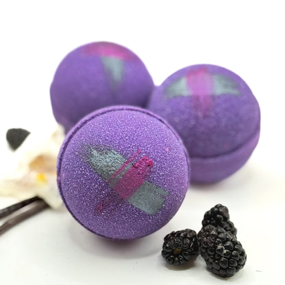 Three purple raspberry vanilla bath bombs with a butterfly design on a white background with blackberries.