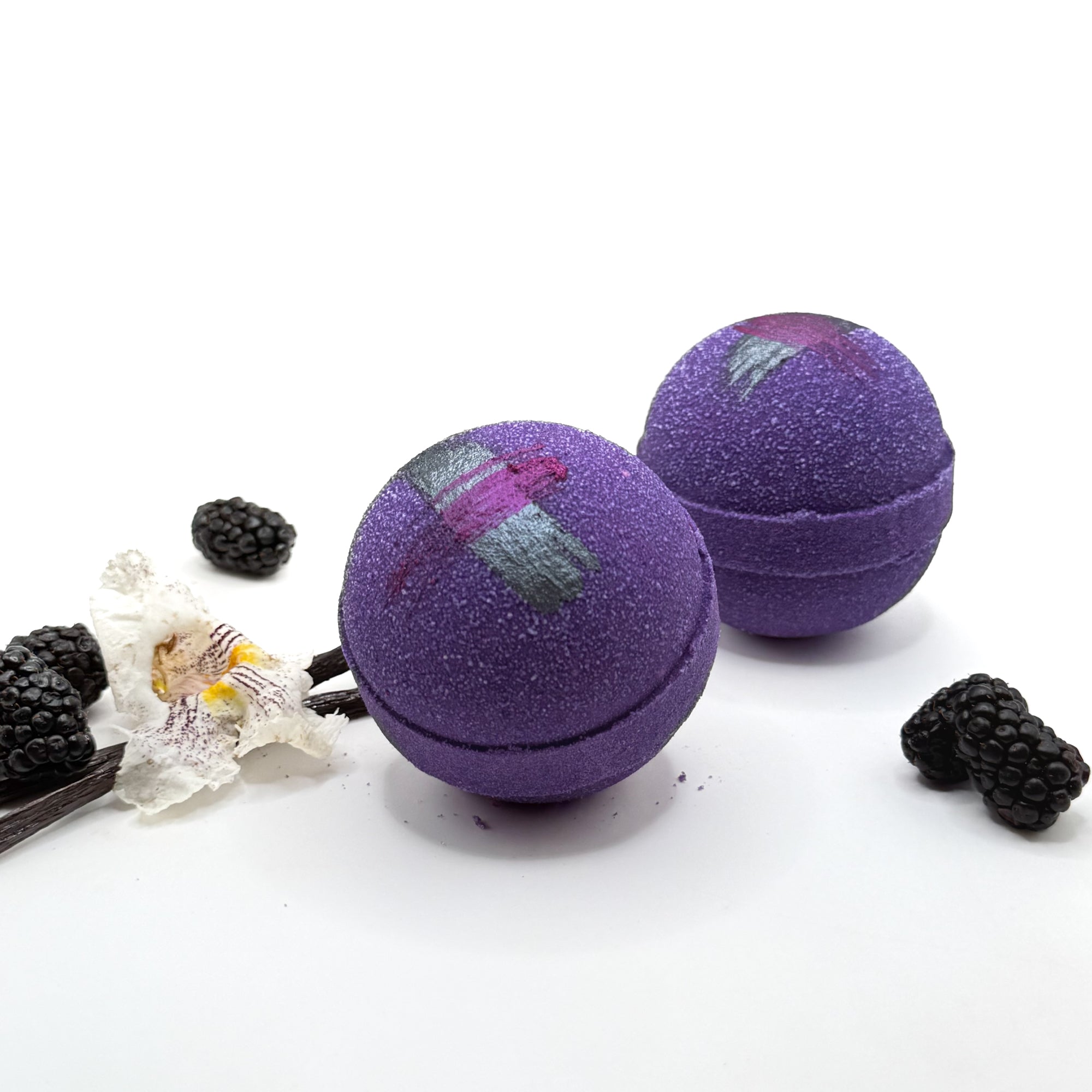 Two purple raspberry vanilla bath bombs with decorative elements on a white background