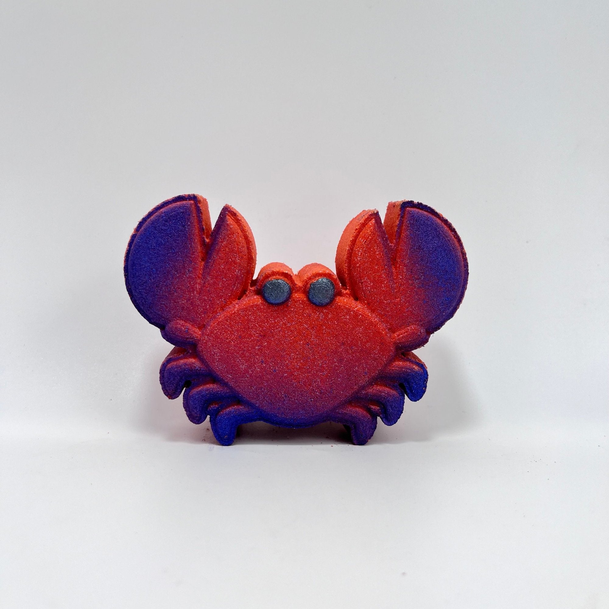 A red crab shaped bath bomb with airbrushed blue claw tips and hand-painted black eyes. 