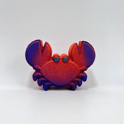A red crab shaped bath bomb with airbrushed blue claw tips and hand-painted black eyes. 