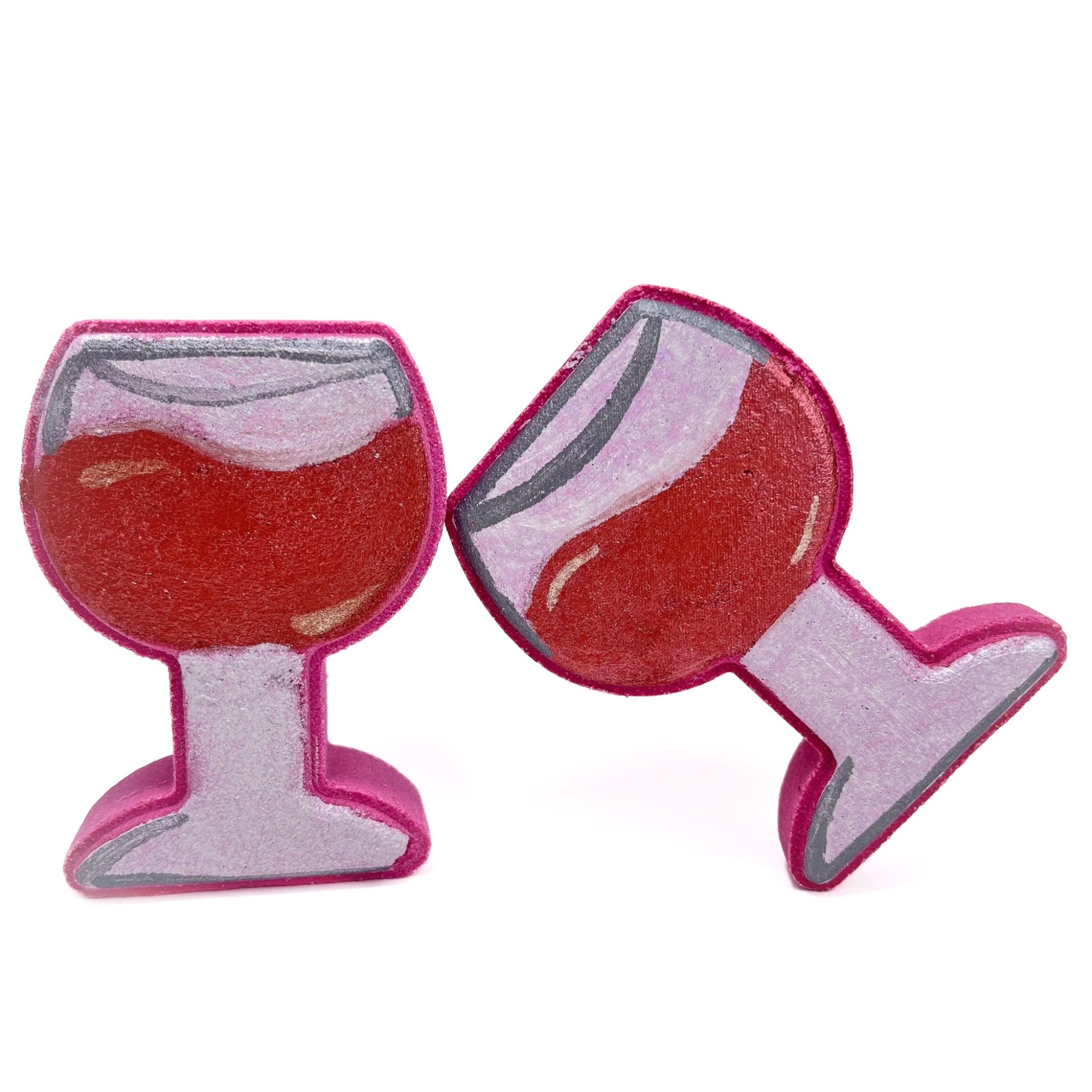 Two hand-painted red wine glass bath bombs from Rusted Acre Soap Co. One upright and one tipping onto the other like cheers!