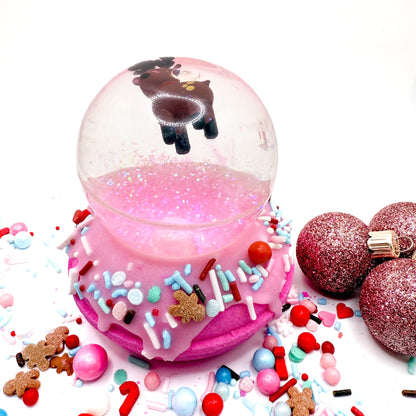 Pink donut bath bomb topped with a reindeer bouncy ball, surrounded by colorful sprinkles on a white background. Handmade by Rusted Acre Soap Co.