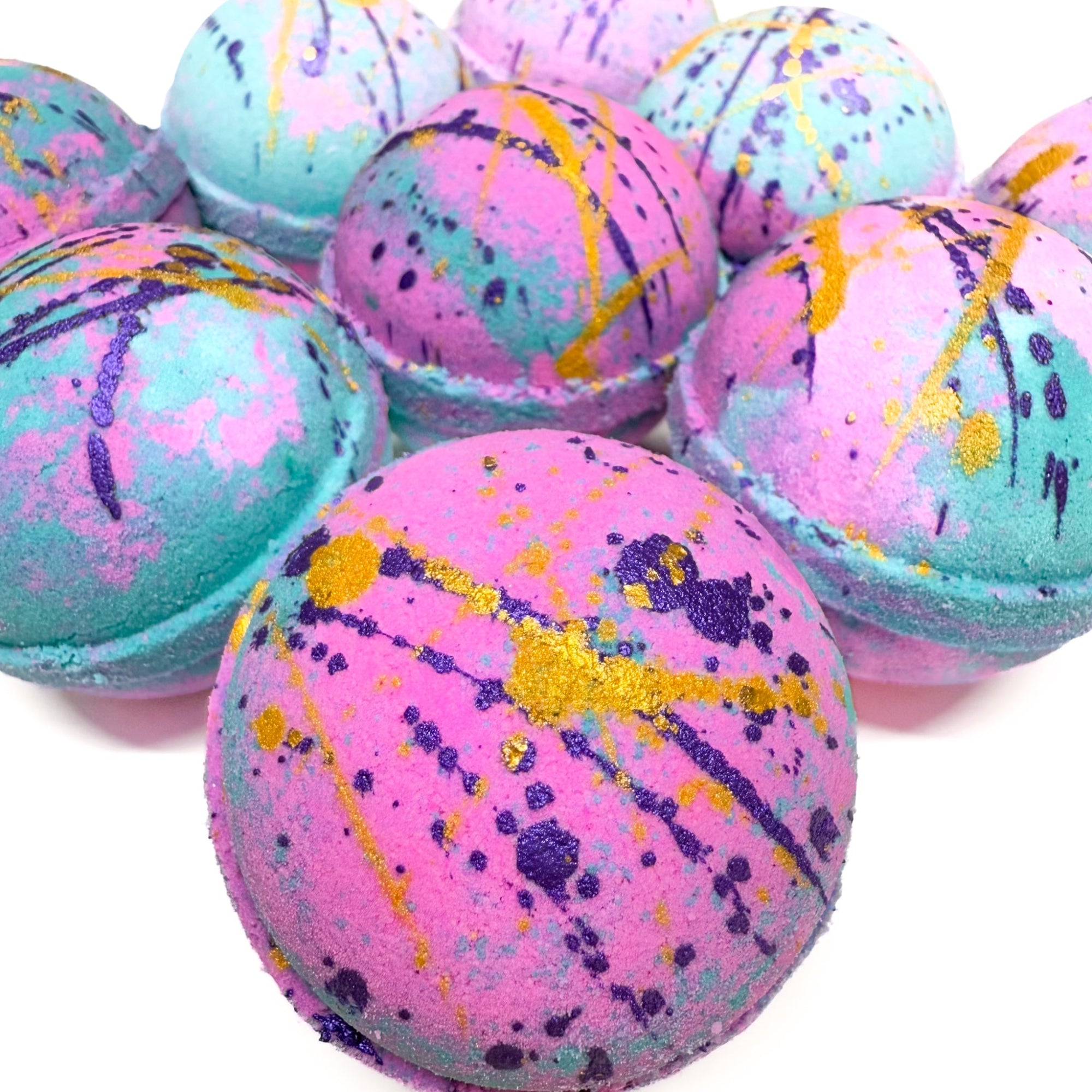 Multiple Pink and Teal bath bombs with purple and gold paint, made by Rusted Acre Soap Company. Scented with a beach aroma. 