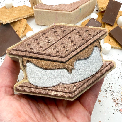 Hand holding a hand painted graham cracker and marshmallow stack bath bomb resembling a s'more.