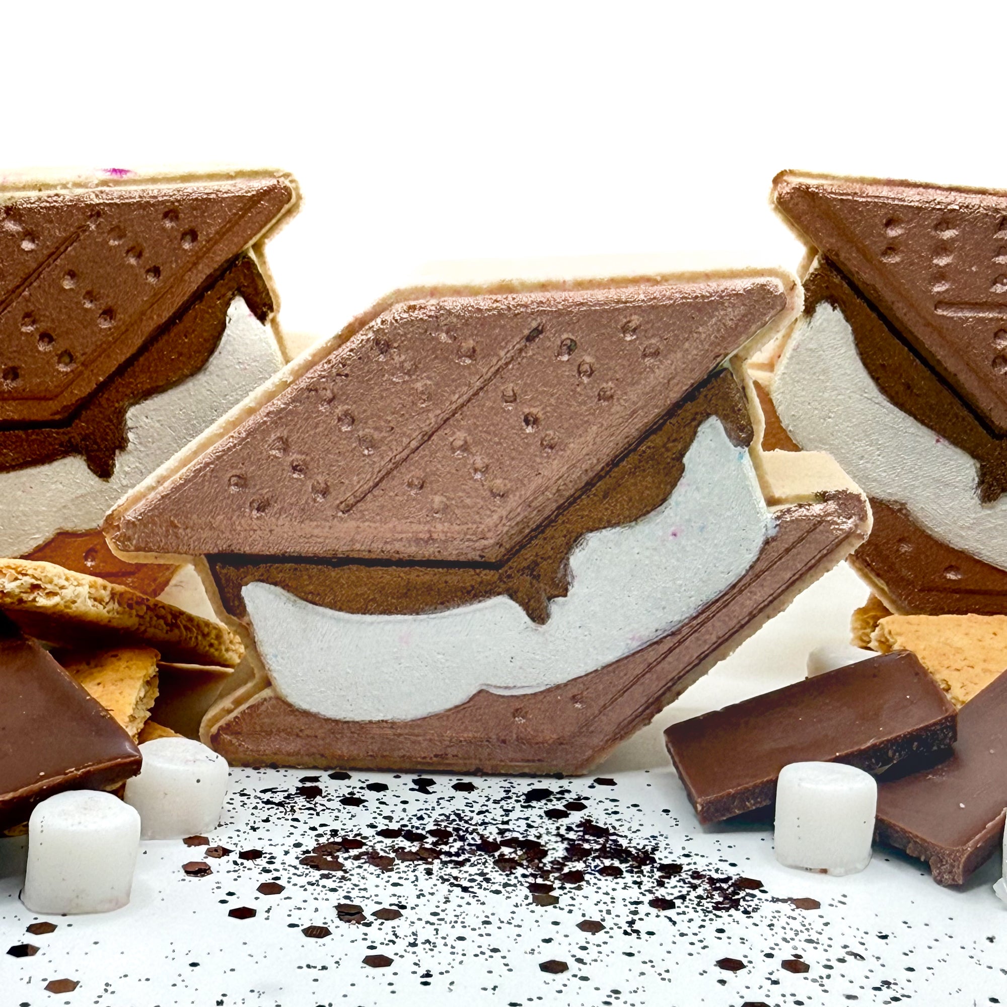 Hand painted Smores shaped bath bomb with s’mores decorations around it on a white background. 