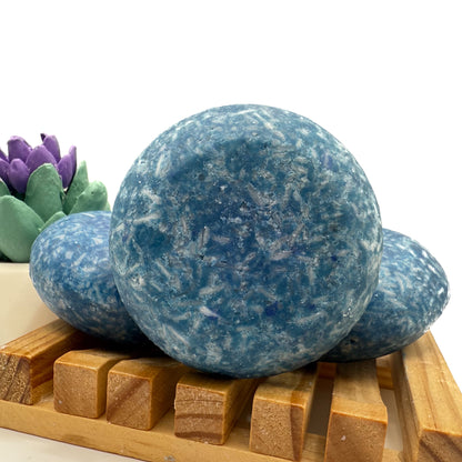 Three blueberry kiss shampoo bars sitting on a wood soap dish two laying flat, one standing up.
